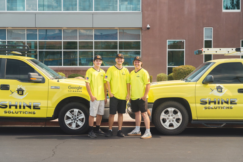 Owner Dyllin, center, with two members of the Shine Solutions crew in lime uniforms, standing between two lime Shine Solutions trucks