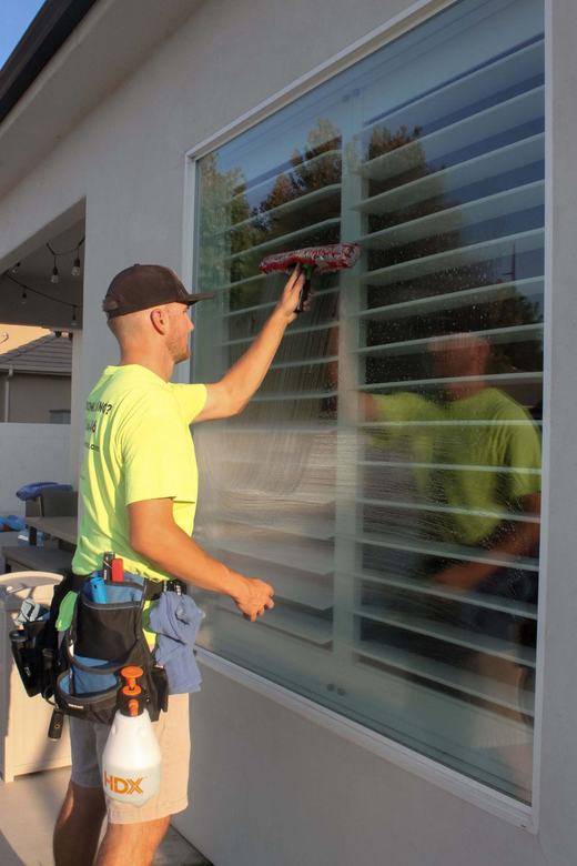 Technician detailing a large window with shutters inside