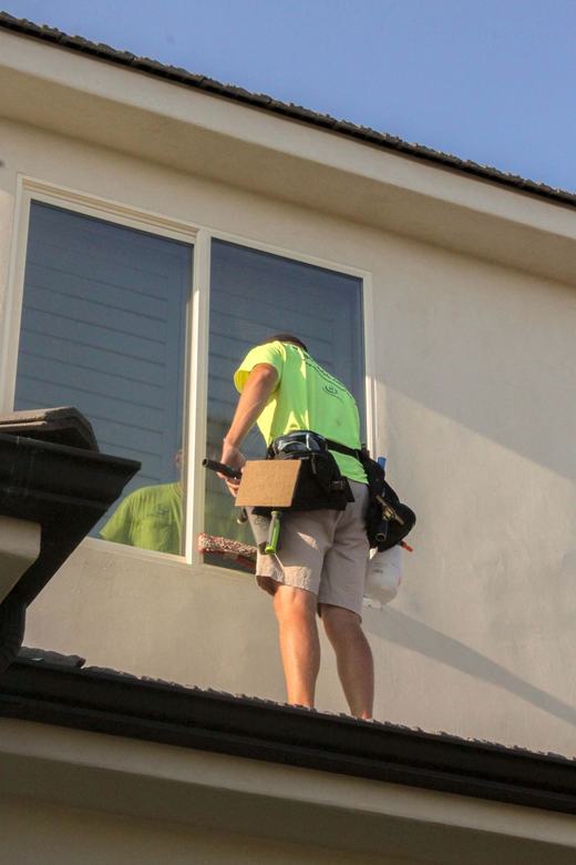 Technician on a roof cleaning a second-story window