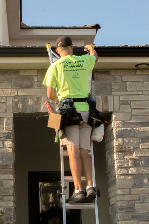 Technician on a ladder cleaning windows above a stone entryway